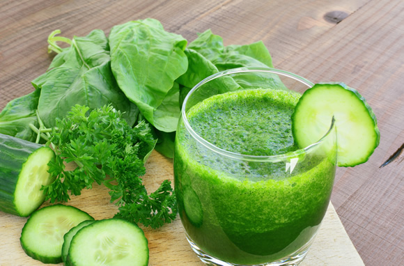 Glass with green drink and cucumber on rim.